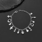 Pulsera con 13 amuletos (2x1 limitado) de plata 925: cruz, luna, corazón, cactus y más; desborda energía positiva. Exhibida sobre fondo negro junto a una piedra texturizada.