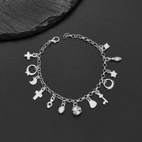 Pulsera con 13 amuletos (2x1 limitado) de plata 925: cruz, luna, corazón, cactus y más; desborda energía positiva. Exhibida sobre fondo negro junto a una piedra texturizada.