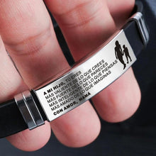 Cargar imagen en el visor de la galería, Primer plano de una mano sosteniendo la Pulsera con dedicatoria &quot;Madre a hijo&quot;, de acero inoxidable, grabada en español: &quot;A MI HIJO: TU ERES MAS VALIENTE DE LO QUE CREES... CON AMOR, MAMA&quot;. Incluye silueta de madre e hijo.