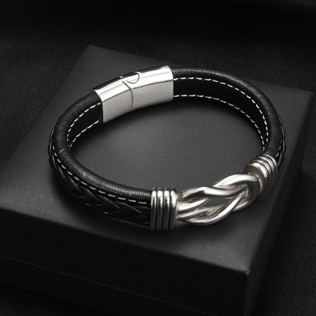 Pulsera con nudo infinito personalizable - A mi hijo: diseño de cuero negro con costuras blancas, cierre magnético plateado y nudo decorativo en plata, presentada en caja negra. Un regalo elegante y significativo para tu hijo.