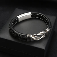 Pulsera con nudo infinito personalizable - A mi hijo: diseño de cuero negro con costuras blancas, cierre magnético plateado y nudo decorativo en plata, presentada en caja negra. Un regalo elegante y significativo para tu hijo.