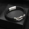 La Pulsera con nudo infinito - A mi hijo es una pulsera de piel negra con costuras blancas, detalle trenzado, cierre plateado y nudo decorativo, perfecta como regalo para hijo o como pulsera especial madre e hijo.
