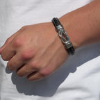Una mano luce la pulsera con nudo infinito personalizable - A mi hijo, de cuero negro con detalles plateados y alambre, ideal como regalo para hijo, sobre una camisa blanca sencilla.