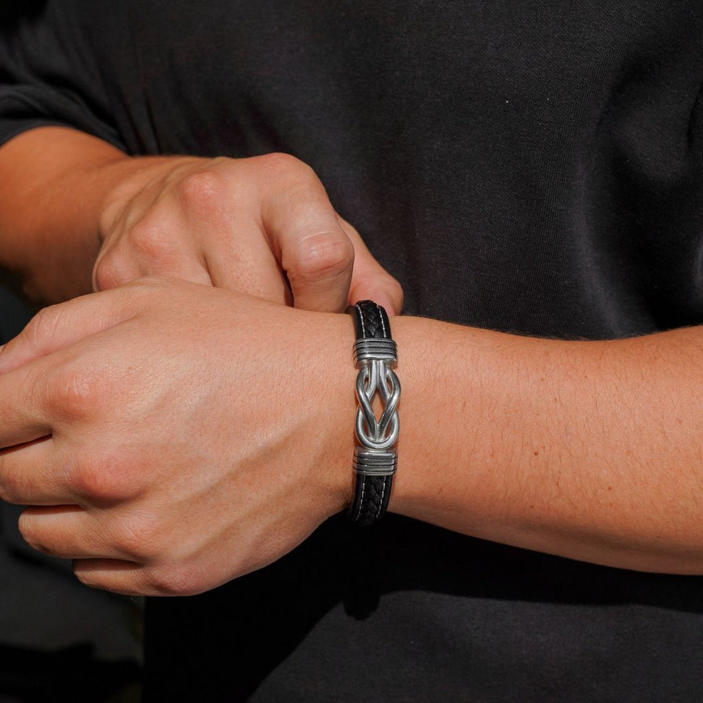 Una persona con camisa negra se abrocha la "Pulsera con nudo infinito personalizable - A mi hijo" alrededor de la muñeca, convirtiéndola en el regalo perfecto para hijo.