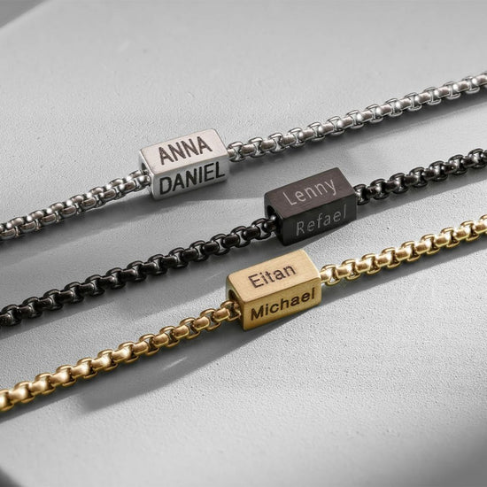 Tres pulseras de cubo personalizadas en plata, negro y dorado se muestran. Cada una tiene un abalorio rectangular grabado con dos nombres, siendo un regalo único para papá y perfecto para el Día del Padre.