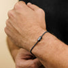 Detalle de una muñeca con la Pulsera de cubo personalizada en negro, de acero inoxidable, con dijes rectangulares grabados DANIEL y AMA. Ideal como regalo personalizado para papá o para el Día del Padre.