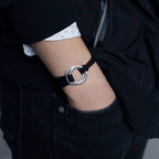 Una persona con jeans y chaqueta negros, camiseta blanca con pequeños estampados, lleva su mano en el bolsillo mostrando una Pulsera de cuerda para hombre grabada; un regalo ideal para él.
