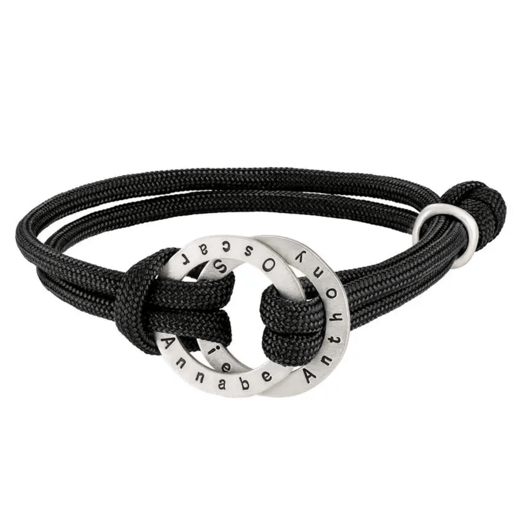 La Pulsera de cuerda para hombre grabada tiene un cordón negro y un colgante circular de plata grabado con los nombres Annabe, Oscar y Antony. El colgante está entretejido en el cordón con un nudo lateral, perfecto como regalo para hombre.
