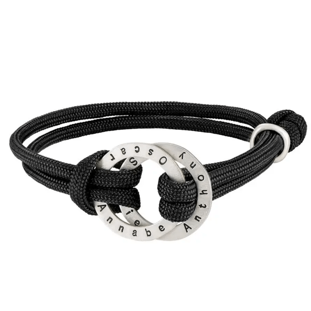 La Pulsera de cuerda para hombre grabada tiene un cordón negro y un colgante circular de plata grabado con los nombres Annabe, Oscar y Antony. El colgante está entretejido en el cordón con un nudo lateral, perfecto como regalo para hombre.