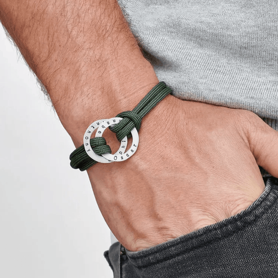Una persona lleva la Pulsera de cuerda para hombre grabada con un colgante redondo plateado, combinándola con unos vaqueros oscuros y una camisa gris claro: un regalo personalizado para hombre ideal.