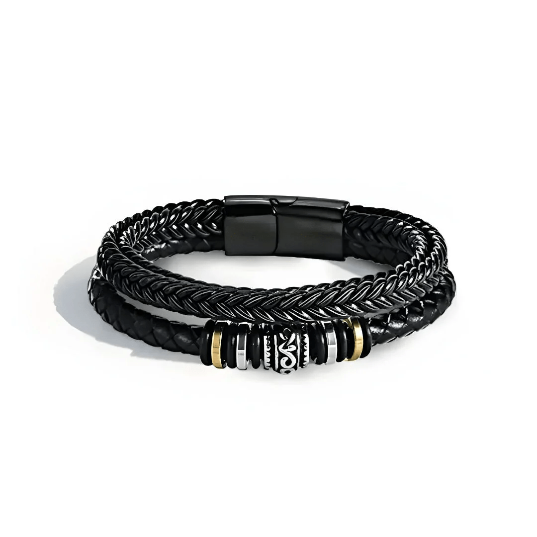 La Pulsera de cuero - Al hombre de mi vida tiene tres bandas de cuero negro trenzado con una pieza central decorativa plateada, negra y dorada y un cierre magnético negro, perfecta como regalo de amor o pulsera personalizada para cualquier ocasión.