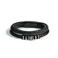 La Pulsera de cuero - Al hombre de mi vida tiene tres bandas de cuero negro trenzado con una pieza central decorativa plateada, negra y dorada y un cierre magnético negro, perfecta como regalo de amor o pulsera personalizada para cualquier ocasión.