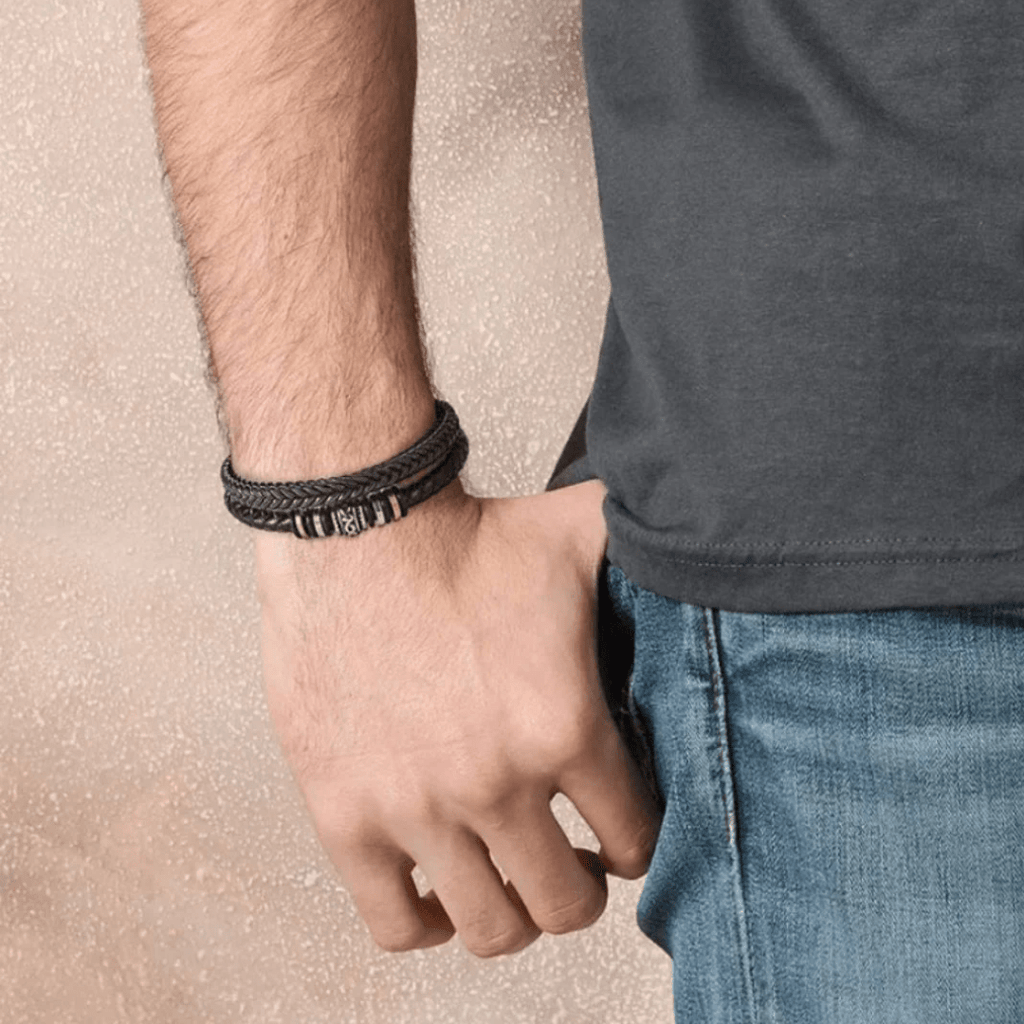 Un hombre con camiseta oscura y jeans azules luce en la muñeca la Pulsera de cuero - Al hombre de mi vida, ideal como regalo especial o pulsera personalizada.