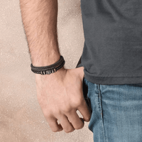 Un hombre con camiseta oscura y jeans azules luce en la muñeca la Pulsera de cuero - Al hombre de mi vida, ideal como regalo especial o pulsera personalizada.