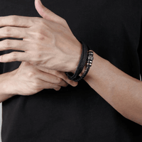 Una persona con camiseta negra ajusta la Pulsera de cuero - Al hombre de mi vida con detalles metálicos en su muñeca, mostrando esta pulsera personalizada como el regalo de amor perfecto para cualquier ocasión. Sólo se ven sus manos y parte de sus brazos.