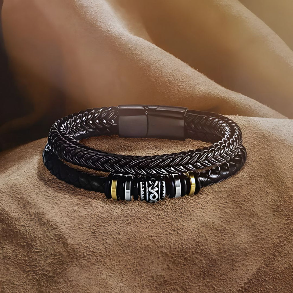 La pulsera de cuero "Siempre contigo Papá" para hombre, con elegantes detalles metálicos en tonos plata y oro, se exhibe sobre suave tela marrón bajo luz cálida; un regalo ideal para padres.