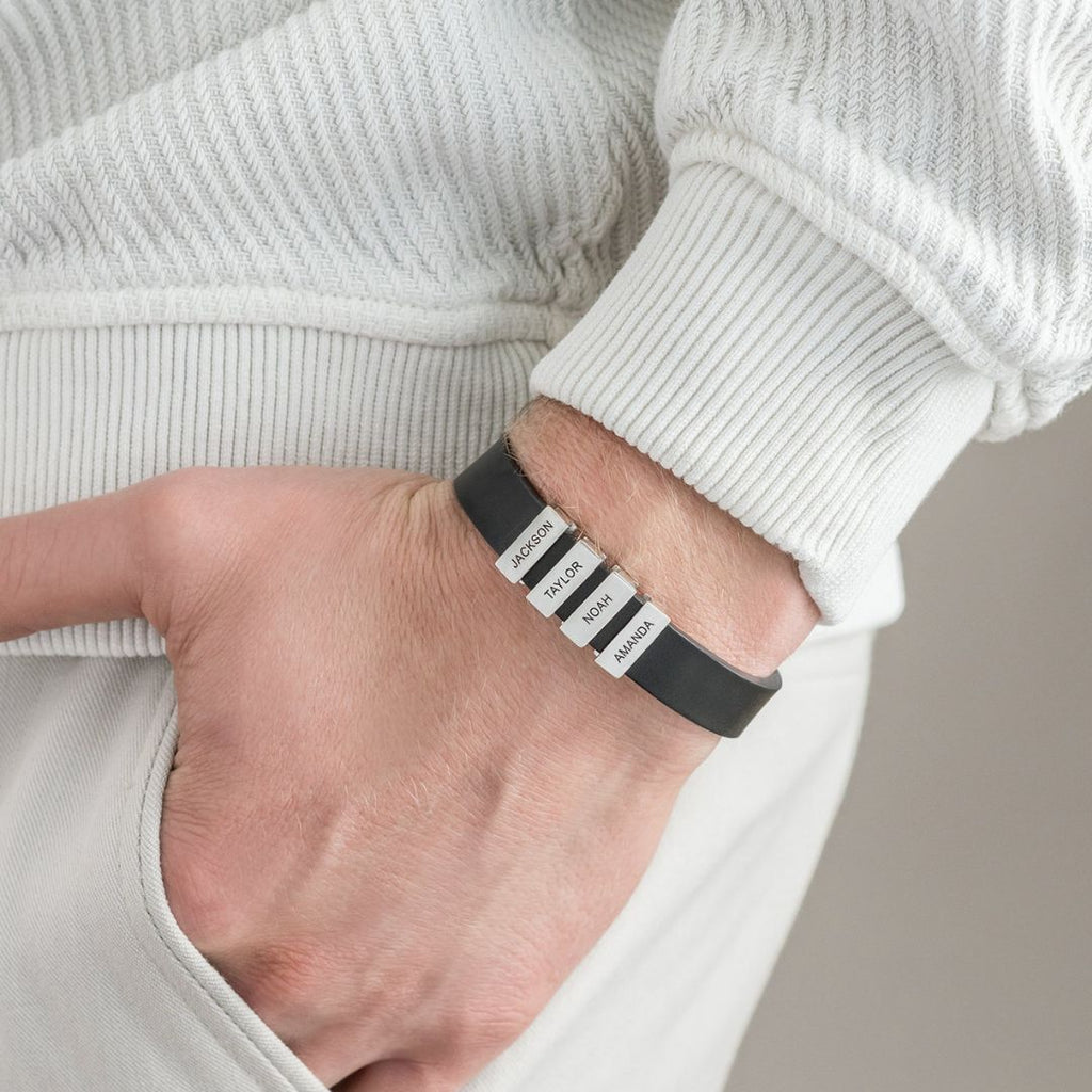 Una persona vestida con ropa de color claro tiene la mano en el bolsillo, mostrando una Pulsera de hombre con nombres grabados con cuatro etiquetas blancas-JACKSON, MASON, HENRY, y MADISON-un regalo ideal original hombre.