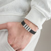 Una persona vestida con ropa de color claro tiene la mano en el bolsillo, mostrando una Pulsera de hombre con nombres grabados con cuatro etiquetas blancas-JACKSON, MASON, HENRY, y MADISON-un regalo ideal original hombre.