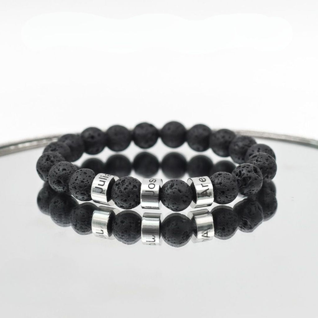 A Pulsera de piedra volcánica personalizada, con cuentas negras que simulan roca volcánica y letras plateadas formando una palabra, ideal como pulsera personalizada para papá o un regalo especial para el Día del Padre.