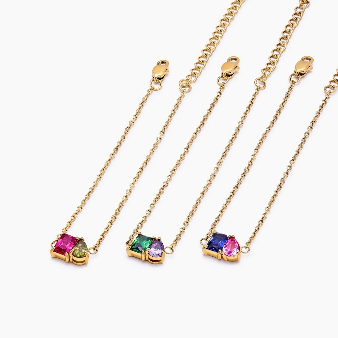 Cuatro pulseras dos mitades con piedras de nacimiento en combinaciones rosa-verde, verde-morado, morado-azul y azul-rosa destacan sobre fondo blanco.