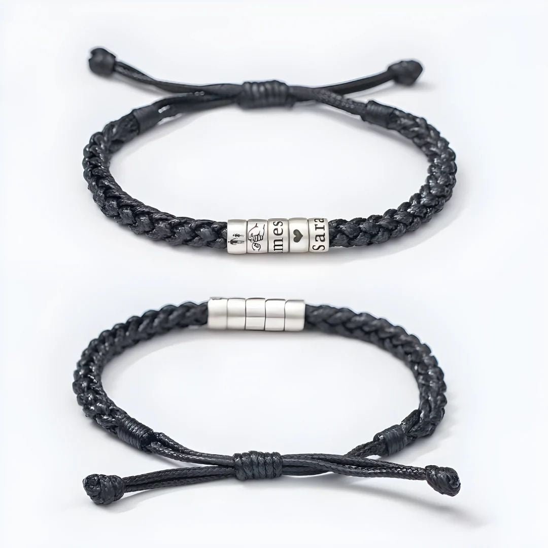 Dos pulseras negras "El mejor Papá" con nudos ajustables sobre fondo blanco: una lleva cuatro cuentas plateadas grabadas con caras de dibujos animados y "Tiempos tristes", mientras que la otra lleva cuentas plateadas lisas. Ambas son totalmente personalizables.