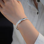 Una persona con camisa blanca luce en su muñeca la Pulsera Elegancia Real, un brazalete de acero inoxidable con un intrincado diseño inspirado en hojas y detalles brillantes.