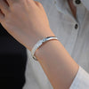 Una persona con camisa blanca luce en su muñeca la Pulsera Elegancia Real, un brazalete de acero inoxidable con un intrincado diseño inspirado en hojas y detalles brillantes.