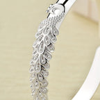 Primer plano de la Pulsera Elegancia Real, fabricada en acero inoxidable con intrincados motivos de plumas y piedras brillantes, sobre un fondo neutro.