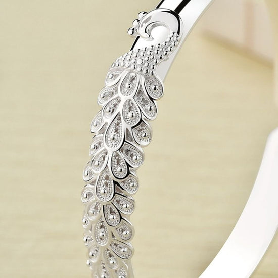 Primer plano de la Pulsera Elegancia Real, fabricada en acero inoxidable con intrincados motivos de plumas y piedras brillantes, sobre un fondo neutro.