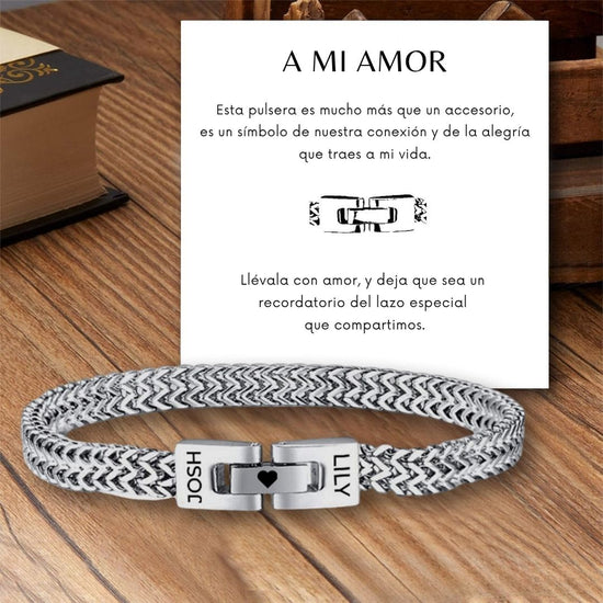 Una Pulsera grabada en plata y negro - A mi amor con JOSH y LILY grabados descansa sobre madera. Detrás de esta pulsera personalizada hay un sentido mensaje en español sobre una caja de madera y un libro-regalo perfecto para hombre.