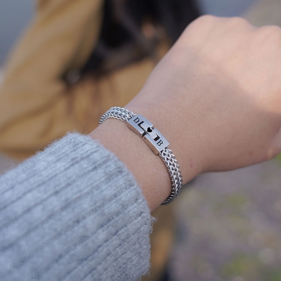 Primer plano de una muñeca con la Pulsera grabada - A mi amor, una pulsera de cadena de plata grabada con un mensaje especial. En el fondo difuminado se ve a alguien con una chaqueta marrón, lo que la convierte en un regalo ideal para hombre.