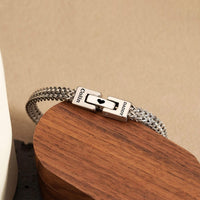 A pulsera grabada - A mi amor en plata con cierre entrelazado, grabado "DADDY" y "COOL", expuesto en madera curvada sobre fondo beige-un regalo ideal para hombre.