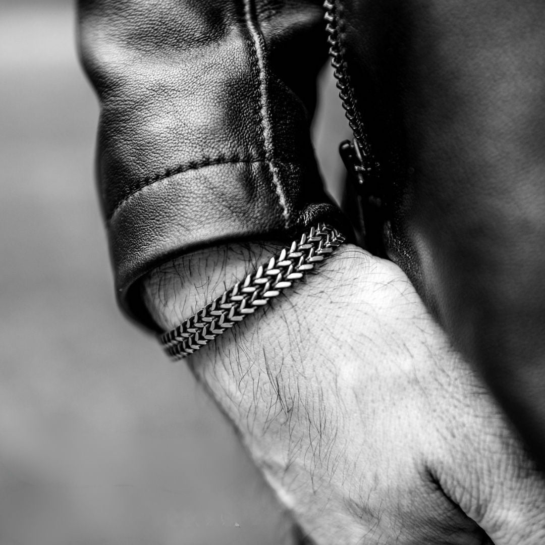 Una foto en primer plano en blanco y negro muestra la mano de un hombre en el bolsillo, con una chaqueta de cuero y la Pulsera grabada - A mi amor, una pulsera con un grueso estampado que es un regalo para hombre lleno de estilo.