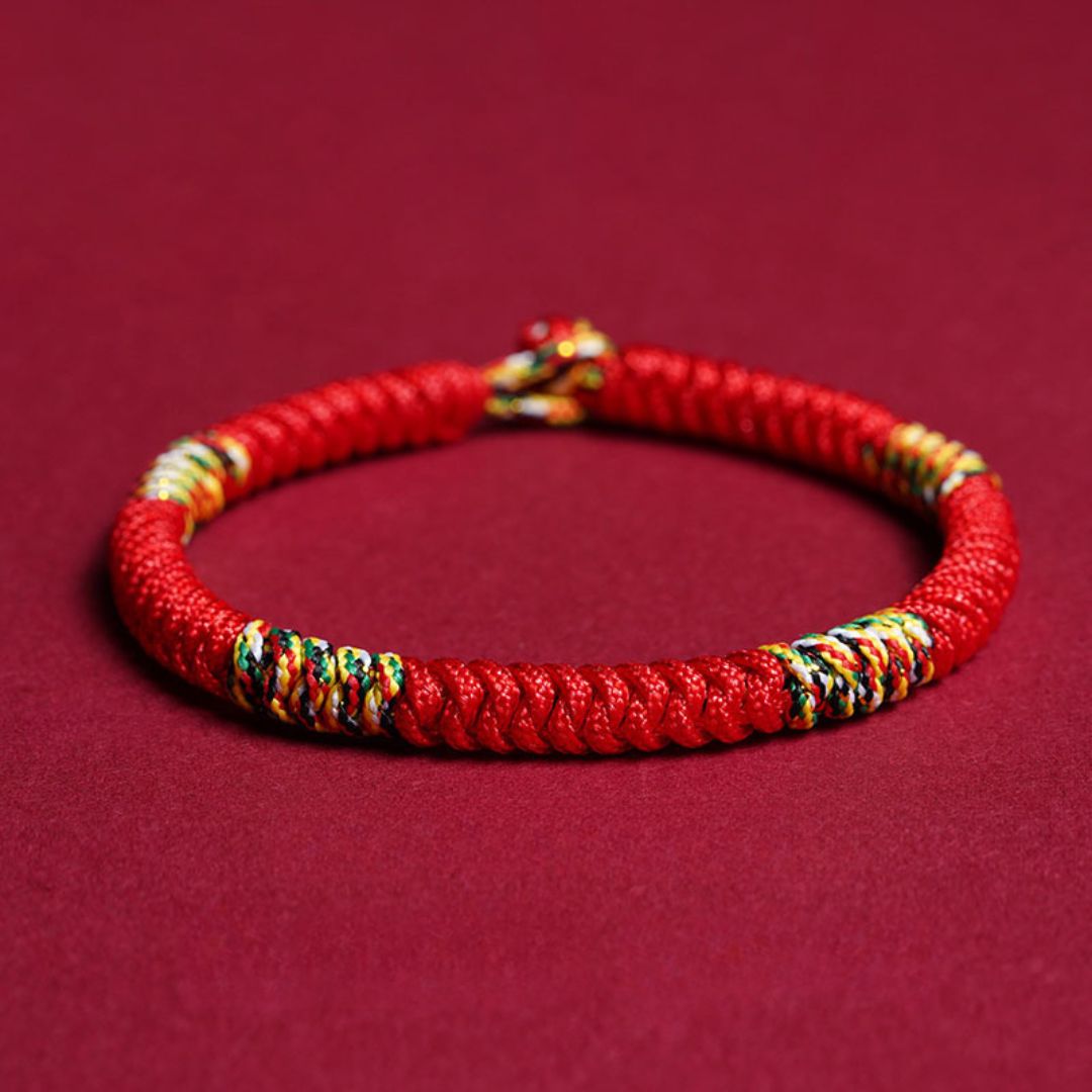 La Pulsera Hilo rojo del destino (Oferta 2X1) es una pulsera trenzada con hilos multicolores sobre fondo rojo, ideal como amuleto de la suerte y protección energética.