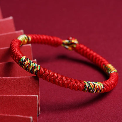 La Pulsera Hilo rojo del destino (Oferta 2X1) luce un trenzado con hilos multicolores, mostrada sobre fondo rojo. Perfecta como amuleto de la suerte y protección energética para usar a diario.