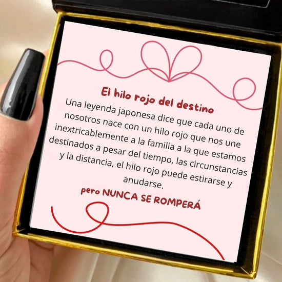 Una mano con las uñas pintadas de negro sostiene una caja abierta que contiene una tarjeta con texto en rojo y una ilustración de una cuerda roja, en la que se explica la Pulsera Hilo rojo del destino (Oferta 2X1), que simboliza conexión y protección energética entre personas destinadas.