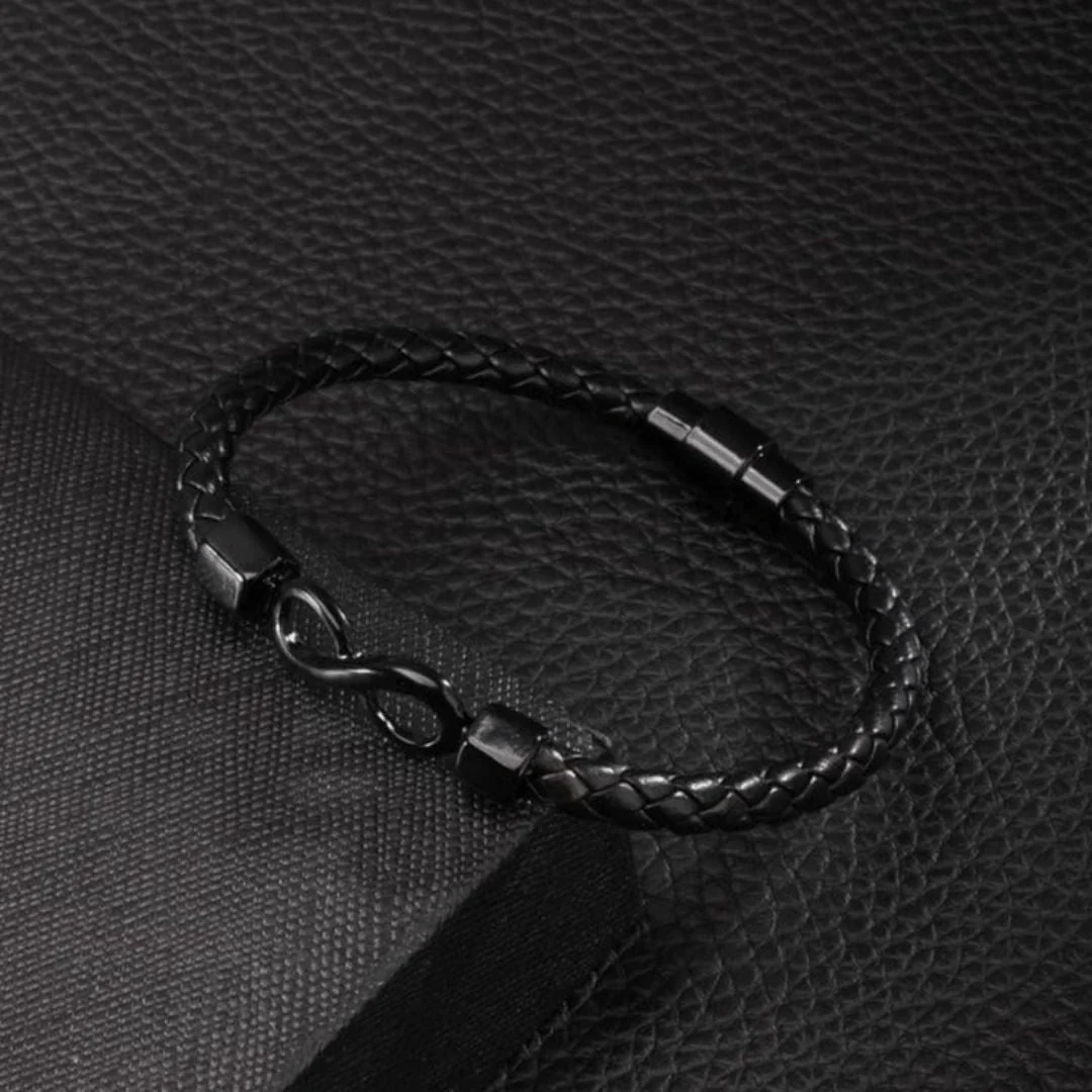 La Pulsera Infinito - A mi hijo es una pulsera de cuero trenzado negro con un elegante cierre infinito de metal negro, que se muestra sobre una superficie negra texturizada: un regalo elegante para su hijo.