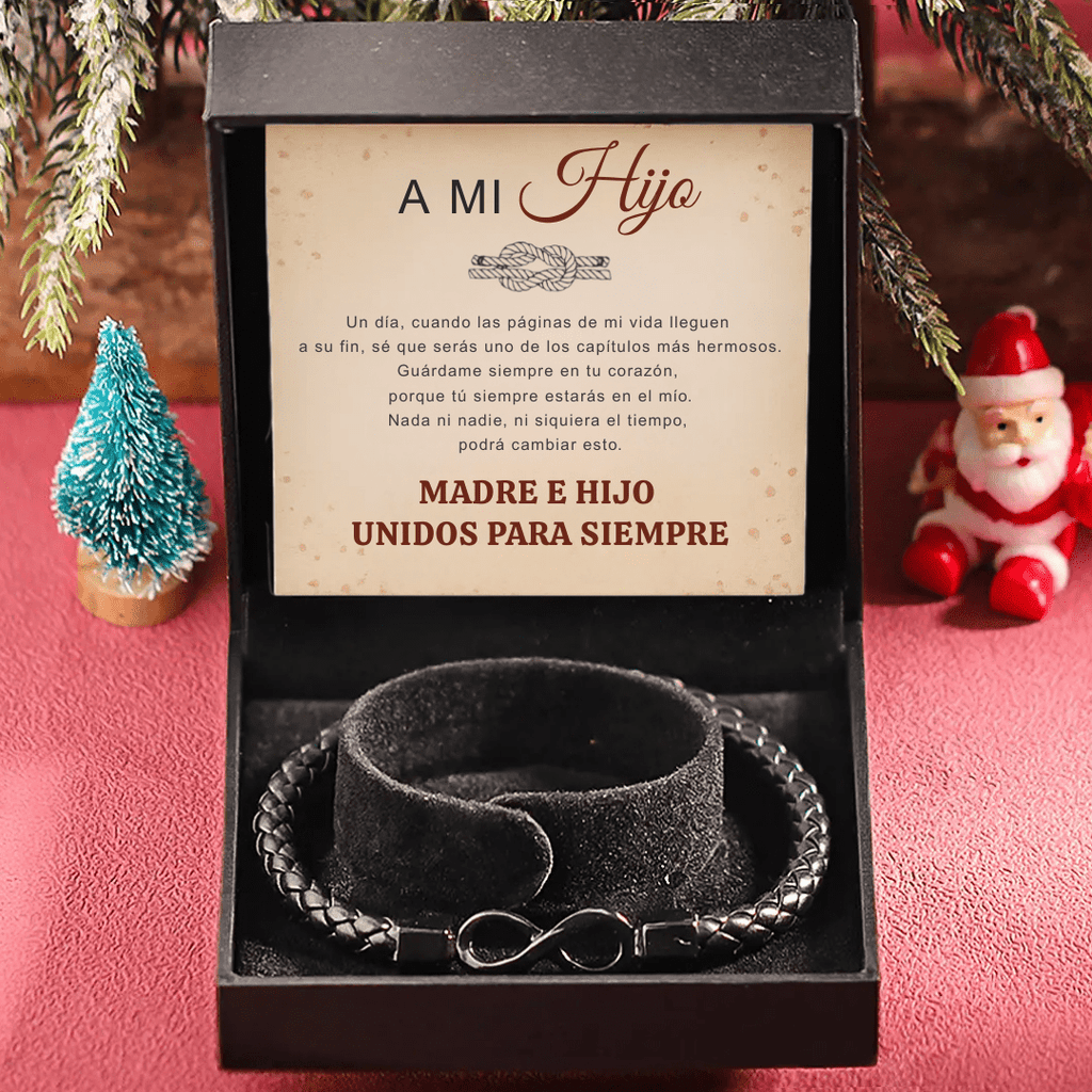 La Pulsera Infinito - A mi hijo es una pulsera de cuero trenzado negro con un charm infinito, presentada en un estuche de regalo. En su interior figura el mensaje en español "Madre e hijo unidos para siempre". Incluye una festiva figurita de Papá Noel-el regalo perfecto para hijo.