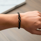Una mano luce la Pulsera Infinito - A mi hijo con charm negro sobre madera, fondo de mármol desenfocado-un regalo elegante e ideal para tu hijo.