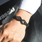 Un primer plano muestra una muñeca que lleva la Pulsera Infinito - A mi Hombre con una pieza central infinita, combinada con una camisa blanca de manga larga. "Waski" aparece en el texto de fondo. Perfecto como regalo para hombre.