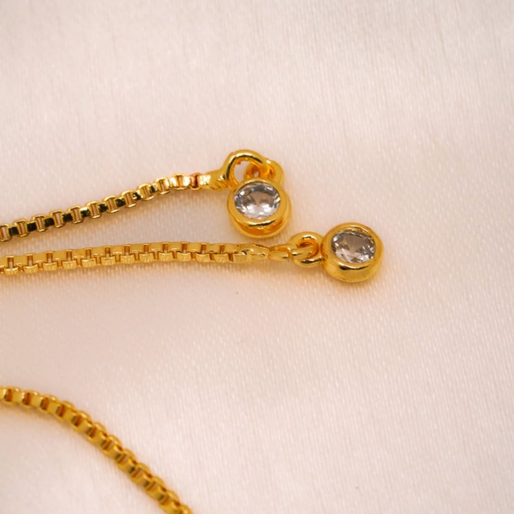 Primer plano de la Pulsera Infinito con ojo turco (OFERTA 2X1), una pulsera de oro con colgantes protectores de ojo turquesa, colocada sobre una tela suave de color claro.