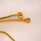 Primer plano de la Pulsera Infinito con ojo turco (OFERTA 2X1), una pulsera de oro con colgantes protectores de ojo turquesa, colocada sobre una tela suave de color claro.