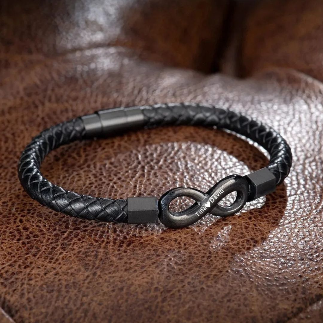 La Pulsera Infinito personalizada - A mi Hombre es una pulsera de cuero trenzado negro con un cierre infinito de metal grabado con texto, desplegado sobre cuero marrón: un regalo ideal para hombre.