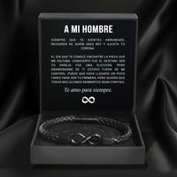 La Pulsera Infinito personalizada - A mi Hombre, una pulsera trenzada negra, se presenta en una caja de regalo negra abierta. Dentro de la tapa hay un sincero mensaje en español titulado "A MI HOMBRE", que la convierte en el regalo perfecto para hombre.