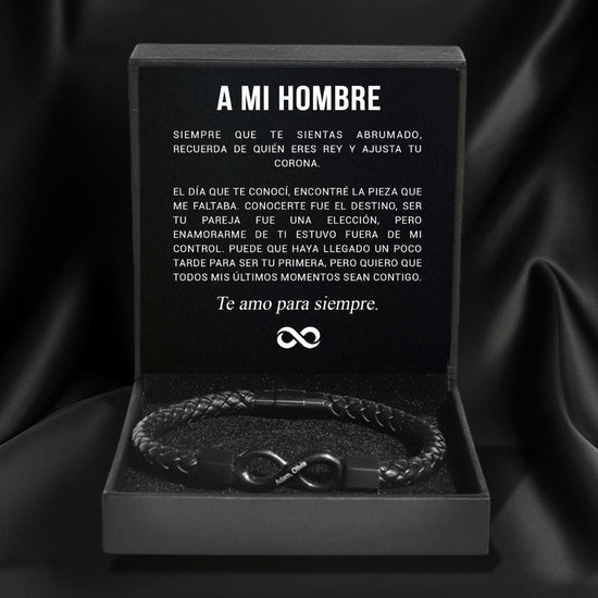La Pulsera Infinito personalizada - A mi Hombre, una pulsera trenzada negra, se presenta en una caja de regalo negra abierta. Dentro de la tapa hay un sincero mensaje en español titulado "A MI HOMBRE", que la convierte en el regalo perfecto para hombre.