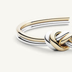 Un primer plano de la Pulsera Nudo infinito dual, una pulsera unisex con bandas de oro y plata entrelazadas en un diseño de nudo, fabricada en acero inoxidable, perfecta como regalo de aniversario.