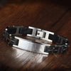 Pulsera personalizada con frase para hombre, hecha de acero inoxidable, con eslabones negros y plateados y placa rectangular cepillada, exhibida sobre superficie de madera oscura.