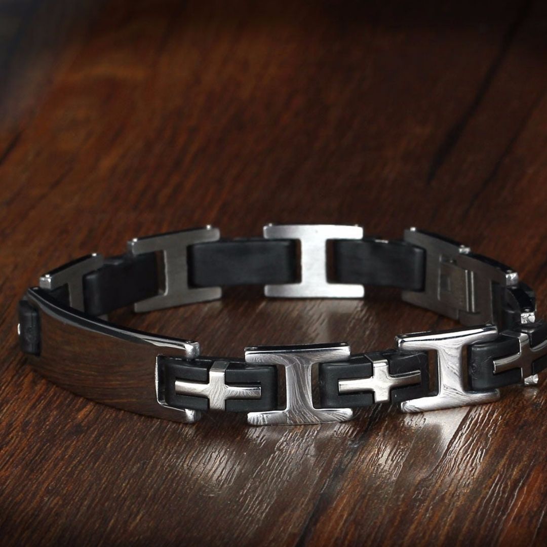 La Pulsera personalizada con frase para hombre, hecha de silicona negra y acero inoxidable plateado con diseños geométricos modernos, se muestra sobre una superficie de madera pulida: un regalo ideal para hombres.