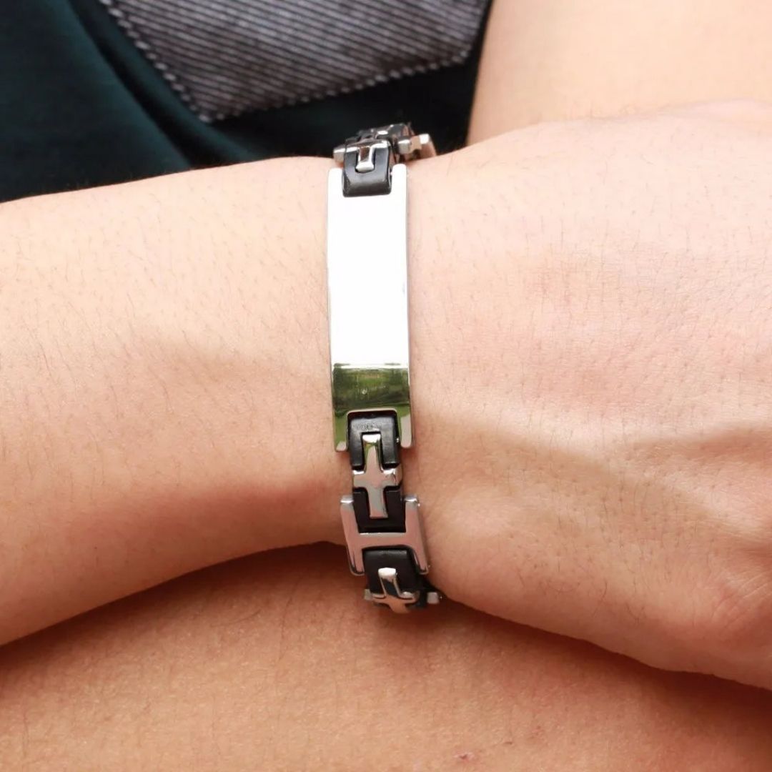 Primer plano de una muñeca que lleva una Pulsera personalizada con frase para hombre, con placa rectangular plateada y diseño de eslabones de cadena negros y plateados: un regalo ideal para hombres.