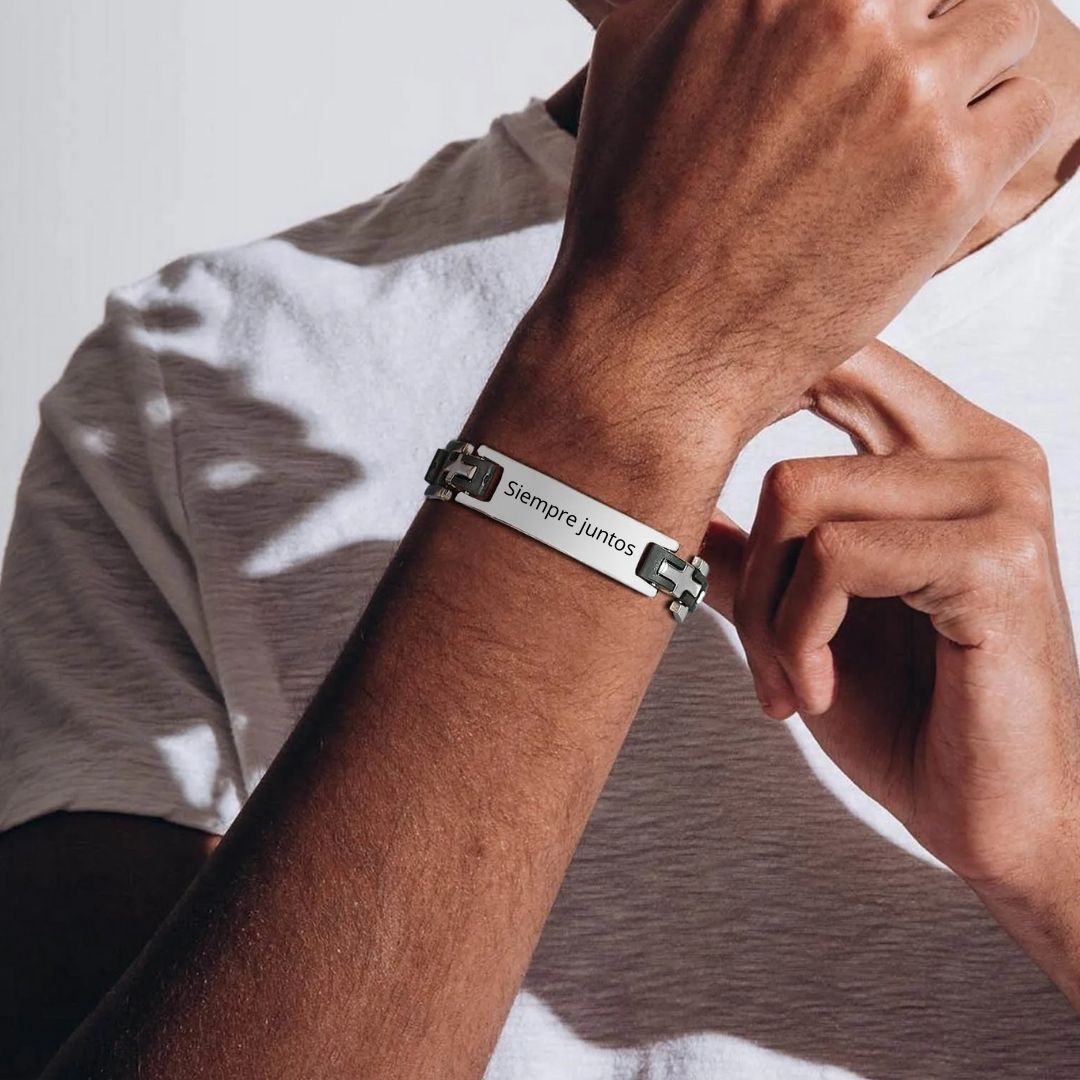 Una persona con camiseta blanca ajusta en su muñeca una Pulsera personalizada con frase para hombre, con una placa rectangular grabada con "Siempre Juntos", lo que la convierte en un regalo ideal para hombres.